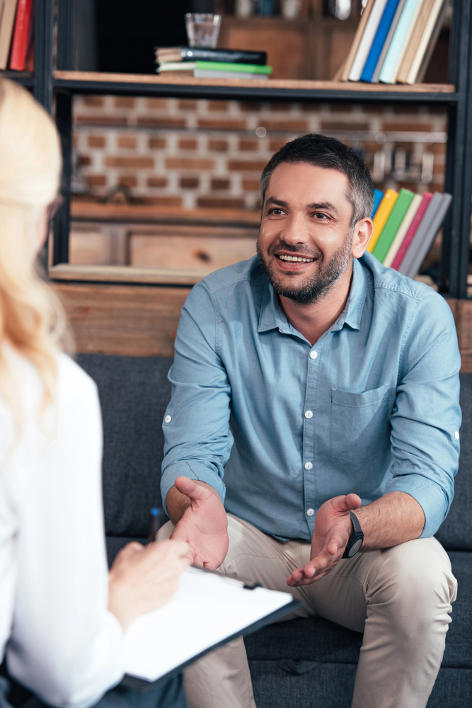 A smiling man in a blue button-down shirt gesturing with his hands while speaking with a professional therapist during a session in Doylestown, PA.